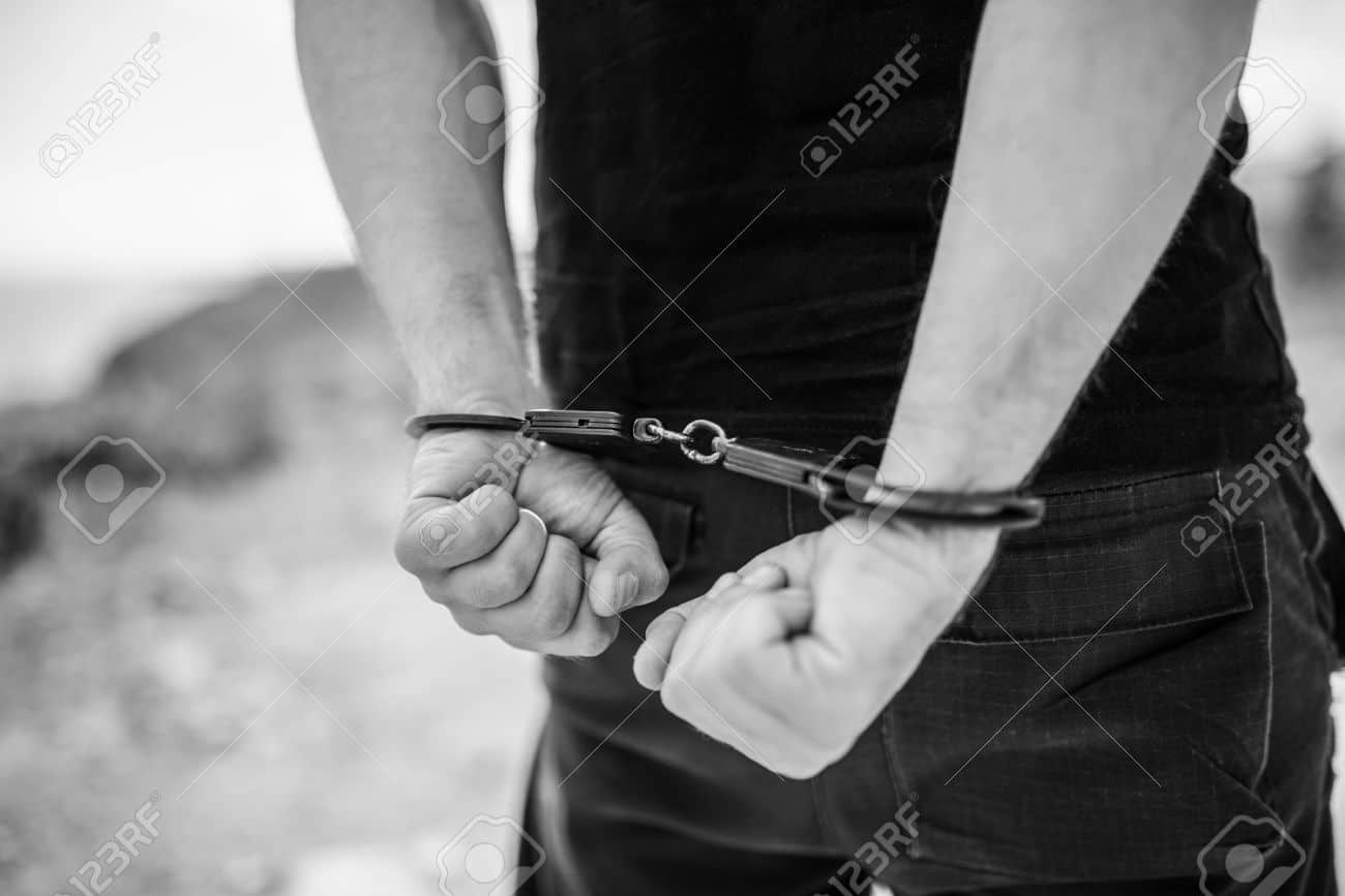52351945-A-mens-hands-in-handcuffs-behind-his-back-Selective-focus-with-shallow-depth-of-field-Black-and-whit-Stock-Photo